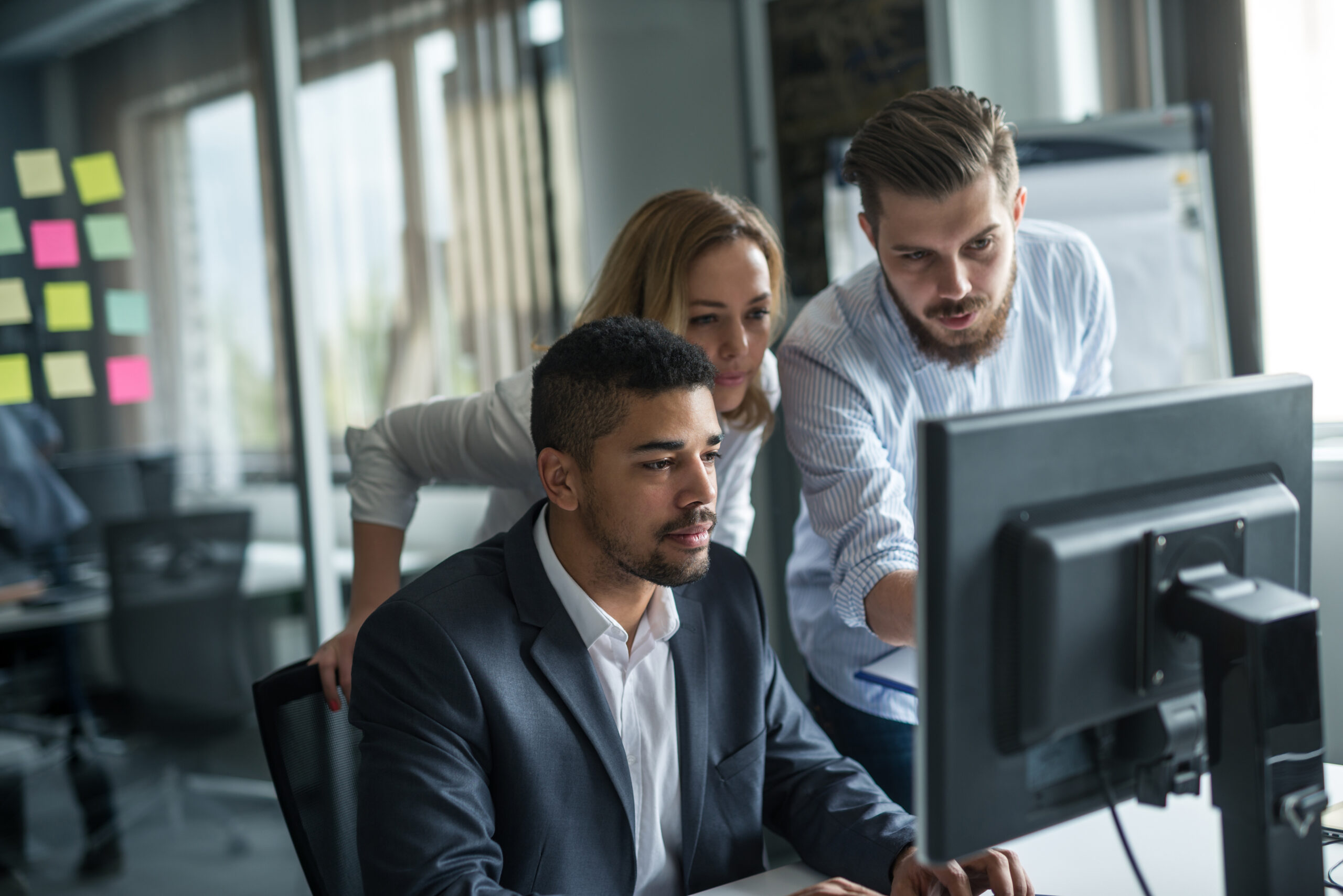 Three business professionals collaborating in an office while working on a computer, illustrating the implementation of IT solutions in a modern workplace.