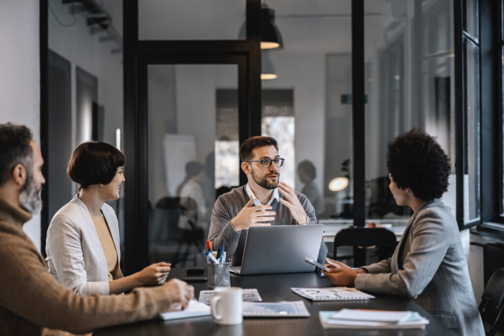 A team of professionals engaged in a discussion around a conference table in a modern office, with a laptop and documents in focus. The collaborative setting highlights the importance of business continuity planning to ensure preparedness and resilience in organizational operations.