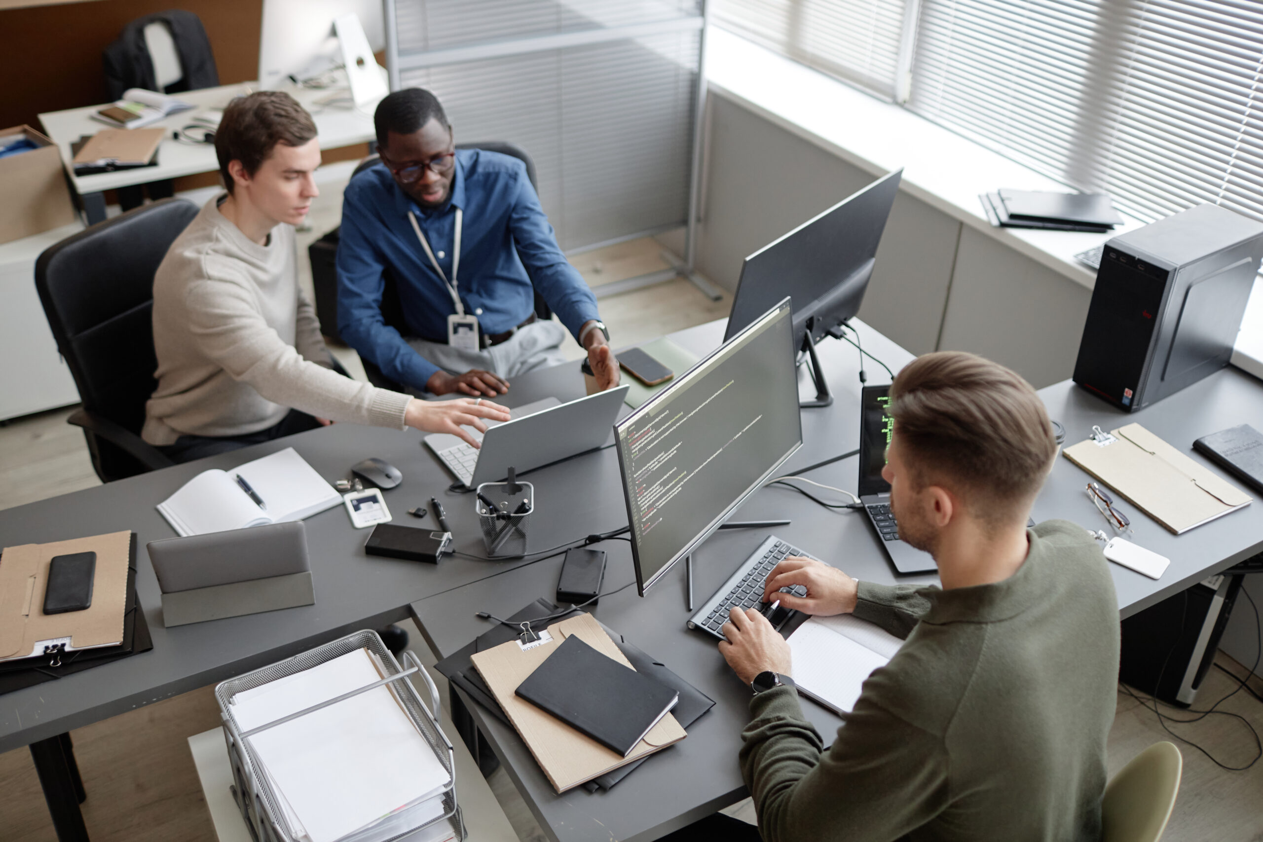 A team of IT professionals collaborating in a modern office, working on multiple screens with coding and data management, representing Managed IT Services.